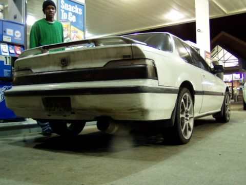1993 Ford Probe - A white coupe with a spoiler is seen from the rear at a gas station. The license plate reads 683-ZPR.