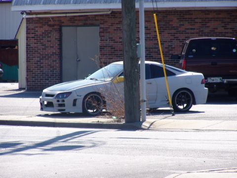 1993 Ford Probe - A modified white coupe sits parked curbside, with a dark pickup truck in the background.