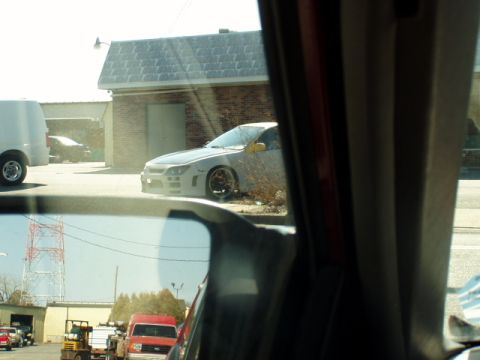 1993 Ford Probe - A modified car sits parked outside a building, with a reflection of traffic in the side mirror.