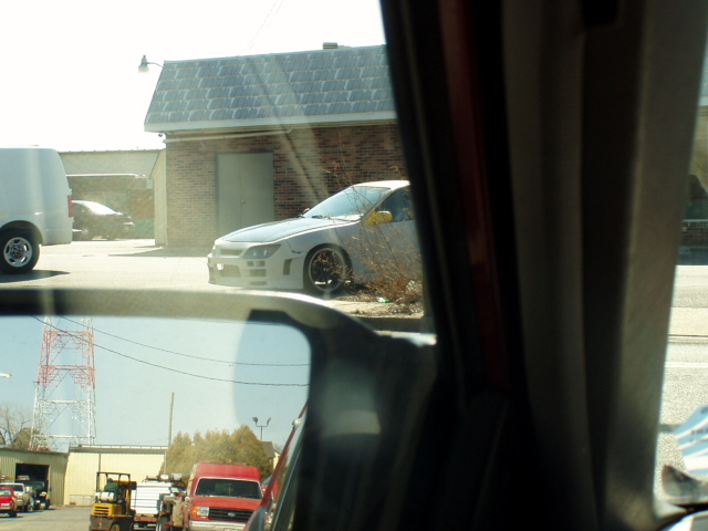 Gray car with aftermarket body kit parked near a brick building, seen from inside another vehicle