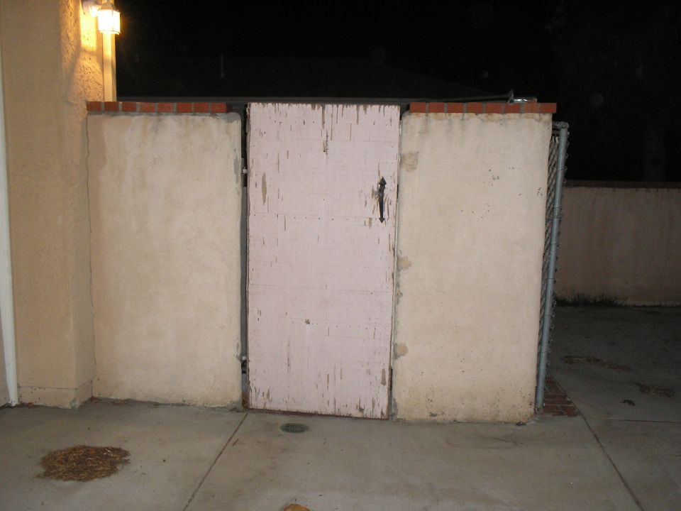 Stucco enclosure with a weathered pink-painted gate at night