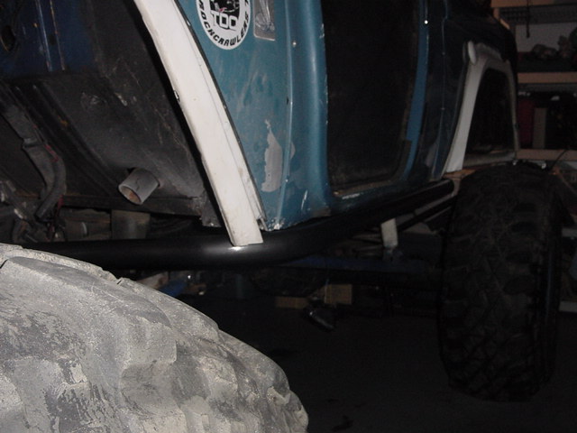 Close-up of a modified off-road vehicle's side, showing large tires, rock sliders, and a sticker on the door