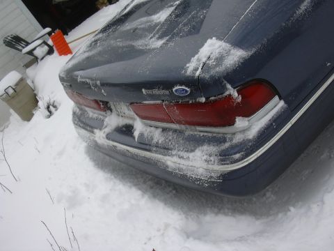 1996 Ford Crown Victoria - Rear view of a dark blue Ford Crown Victoria covered in snow, with a SuperMotors watermark.