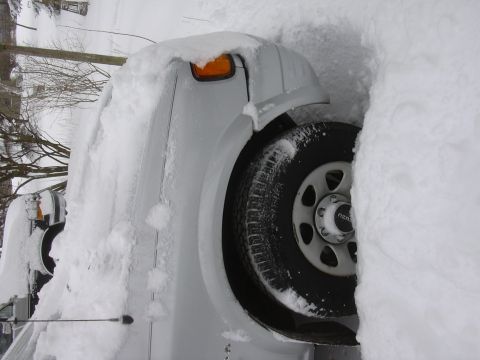1996 Ford Crown Victoria - A white truck is heavily covered in snow, with only a portion of the front and a wheel exposed.