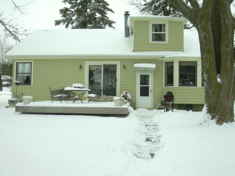 1996 Ford Crown Victoria - A house is covered in snow, with a deck and patio furniture visible on the left.