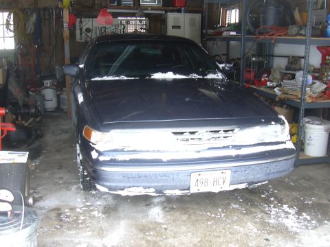 1996 Ford Crown Victoria - A dark sedan is parked in a cluttered garage, with snow visible on its front.