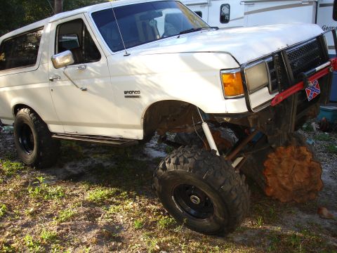 1989 Ford Bronco - A white Ford Bronco is shown with significant suspension lift and off-road tires, parked outdoors.