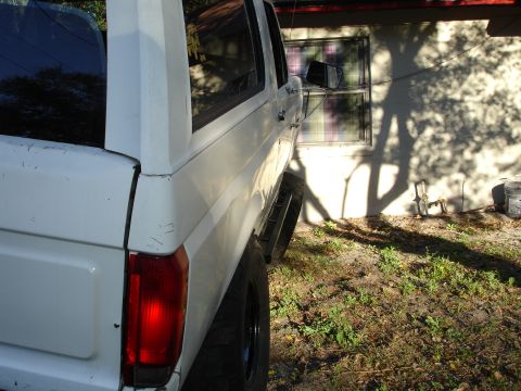 1989 Ford Bronco - A white Ford Bronco is viewed from the rear quarter panel, showing its taillight and side.