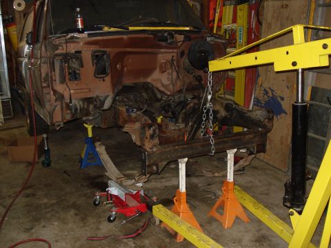 1989 Ford Bronco - A disassembled Ford Bronco sits on jack stands in a garage, awaiting repairs or restoration.