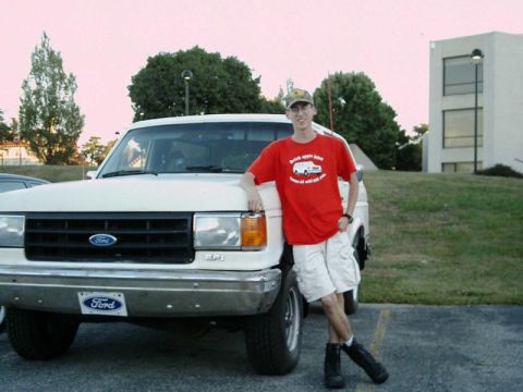 1988 Ford Bronco - A man stands next to a white Ford F-series truck, with a building in the background.