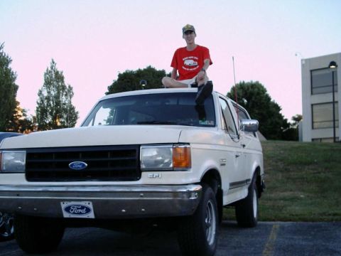 1988 Ford Bronco - A person sits atop a white 1988 Ford Bronco parked outdoors.