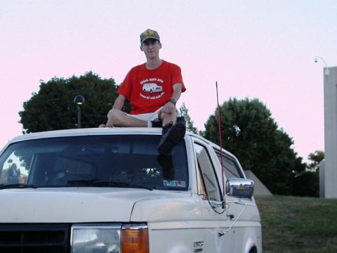 1988 Ford Bronco - A person sits atop a 1988 Ford Bronco, wearing a red t-shirt with a graphic of a vehicle.