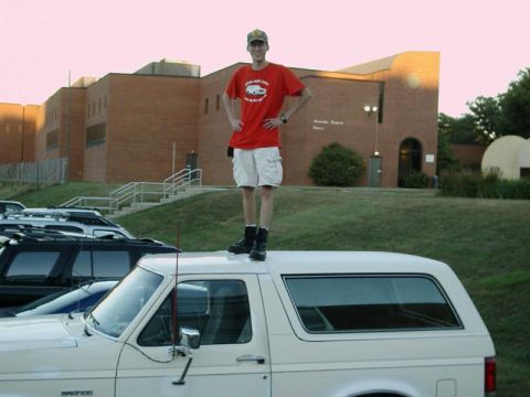 1988 Ford Bronco - A man stands atop a white 1988 Ford Bronco, with other vehicles visible in the background.