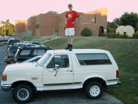 1988 Ford Bronco - Man stands atop a white 1988 Ford Bronco in a parking lot.