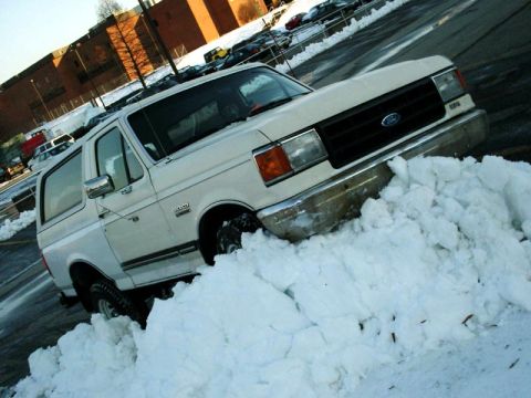 1988 Ford Bronco - A white Ford Bronco is partially buried in a snowdrift in a parking lot.