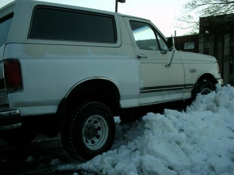1988 Ford Bronco - A white 1988 Ford Bronco is partially buried in a large snowdrift.