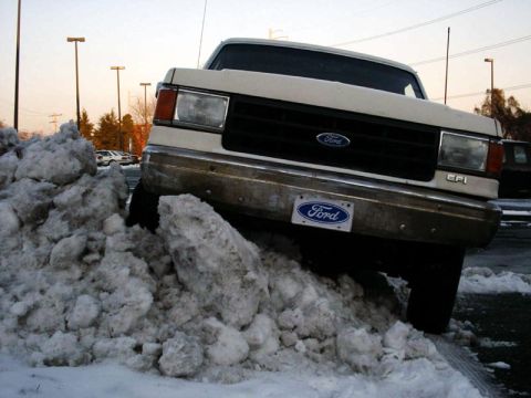 1988 Ford Bronco - A white Ford truck is partially buried in a large snow pile.