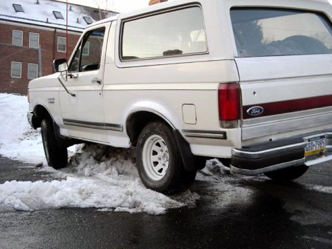 1988 Ford Bronco - A white 1988 Ford Bronco is seen from the rear quarter angle, driving through snow.