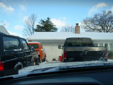 1988 Ford Bronco - A snowy day scene a black SUV, an orange pickup truck, and a black pickup truck parked in a residential driveway.