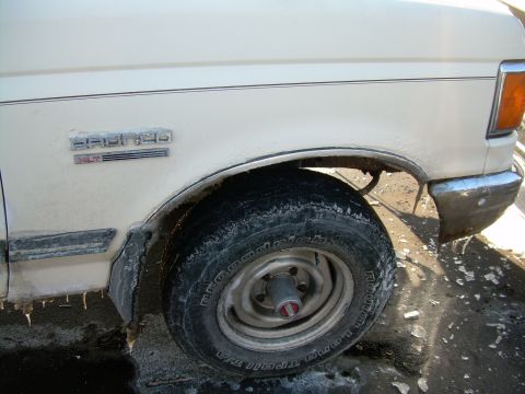 1988 Ford Bronco - Close-up of a white Ford Bronco XLT's front fender and wheel, with snow and ice visible.