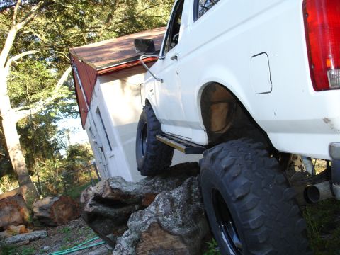 1989 Ford Bronco - A white Ford Bronco is positioned on large rocks, with a small building in the background.