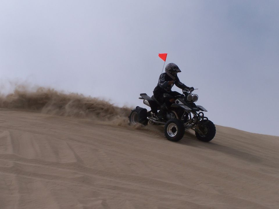 Rider on quad bike kicking up sand while going down a dune