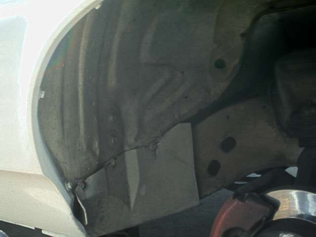 Inner front wheel well of a white car showing bare grey inner fender and red brake part