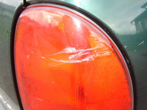 1997 Dodge Grand Caravan - A close-up of a damaged green minivan taillight shows significant scuffing and scratches on the red lens.