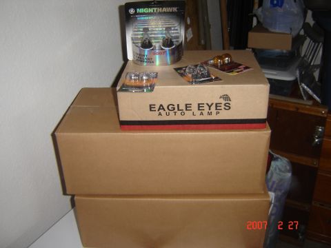 1997 Dodge Grand Caravan - Several boxes of automotive light bulbs are stacked on a shelf in a storage area.