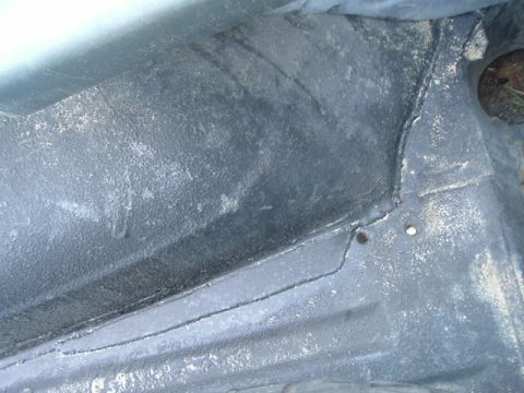 1989 Ford Bronco - The undercarriage of a vehicle shows a black protective coating with visible seams and some wear.