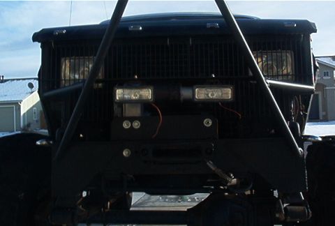 1986 Ford Bronco - Front view of a heavily modified black off-road vehicle, a large grille, winch, and auxiliary lights.
