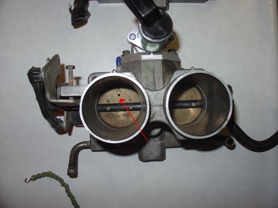 close-up of a dual throttle body with a red arrow pointing to a small hole