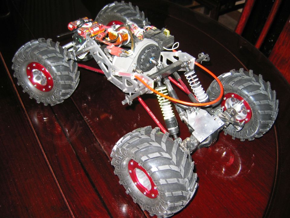 RC rock crawler with aluminum frame, red beadlock wheels and knobby tires on a wood table