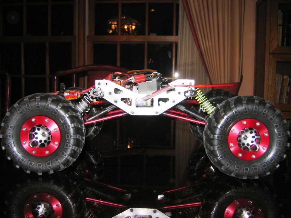 RC rock crawler with red beadlock wheels and white aluminum chassis on glossy surface indoors