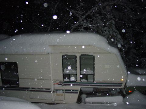 1986 Ford Bronco - A camper trailer sits covered in snow during a winter night, with snowflakes falling.