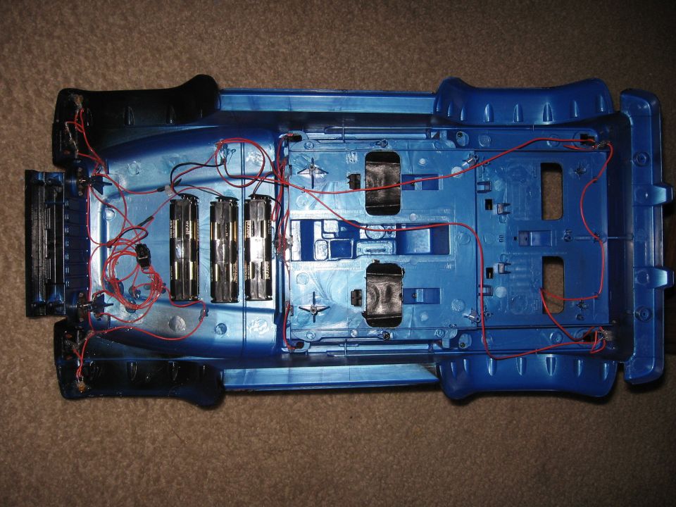 Underside of blue toy truck with wiring and battery compartments