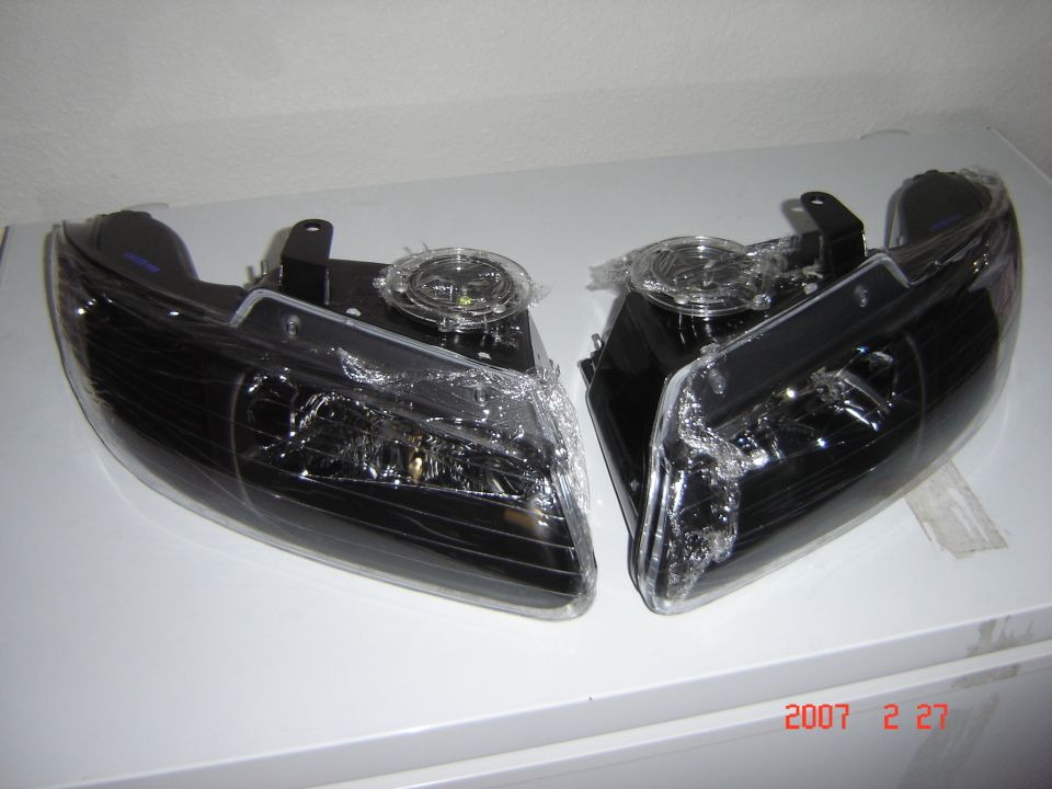 Pair of new black-housing aftermarket headlight assemblies in plastic wrap