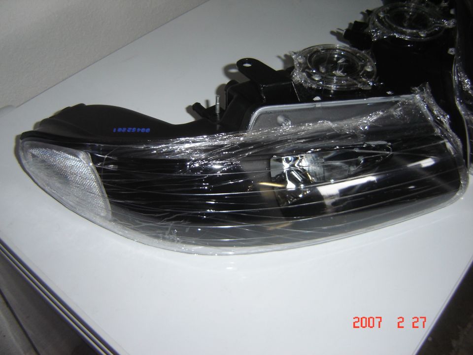 Plastic-wrapped replacement headlight assembly sitting on a white body panel