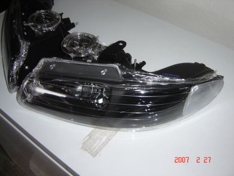 1997 Dodge Grand Caravan - Two new headlights are shown wrapped in protective plastic on a white surface.