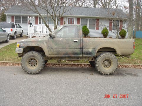 1992 Toyota Tacoma - Side view of a lifted Toyota pickup truck with camouflage paint and off-road tires.
