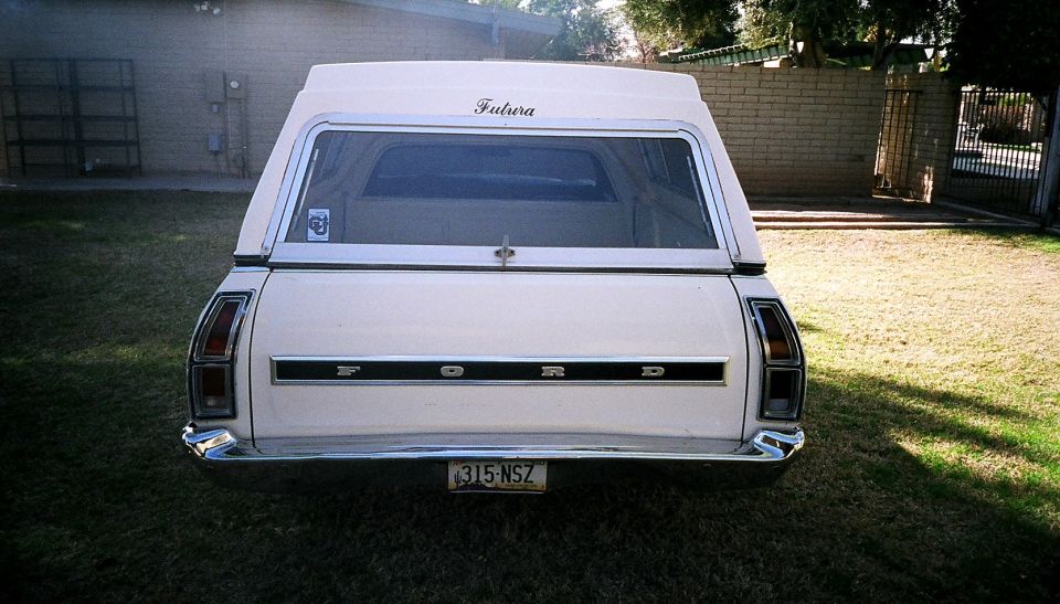 Rear of white Ford with camper shell and 'FORD' tailgate lettering on grass