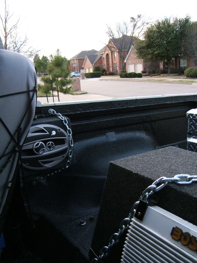 1991 Ford Bronco - The interior of a truck bed shows a speaker and a subwoofer secured with chains.