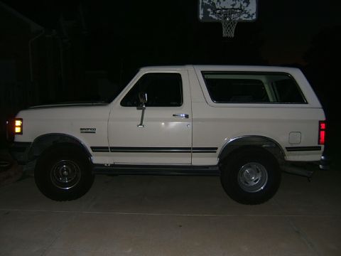 1991 Ford Bronco - A white 1991 Ford Bronco is shown from the side, parked outdoors at night with a basketball hoop visible above.