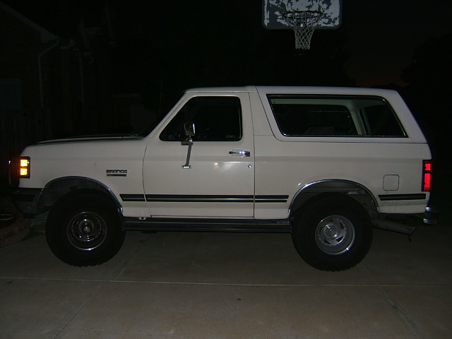 White 1991 Ford Bronco parked on concrete, side view, with a basketball hoop in the background