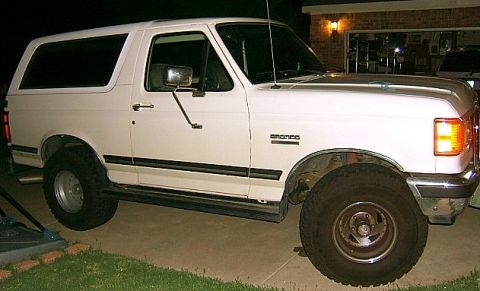 1991 Ford Bronco - This white Ford Bronco is parked in front of a garage at night. The "Bronco" badge is visible on the fender.