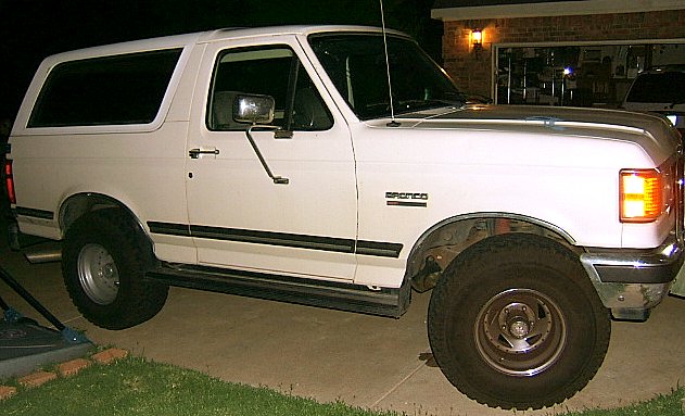 White Ford Bronco parked in driveway at night. Bronco badge visible on fender