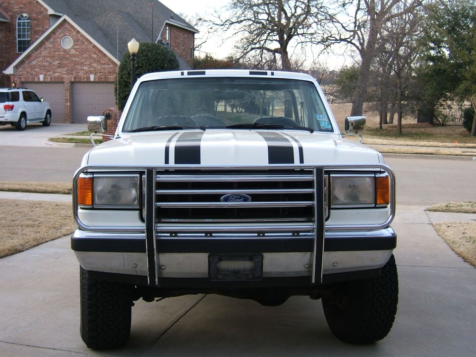White lifted Ford truck front view with hood stripes and chrome grille guard on driveway
