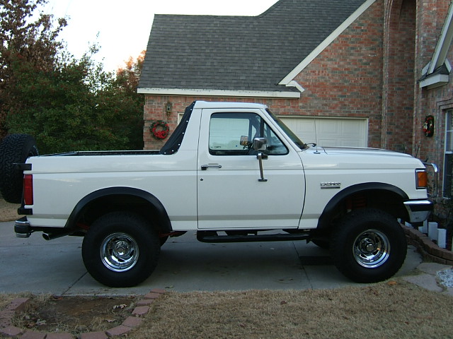 White 1991 Ford Bronco, side view, with a black soft top and spare tire mounted on the rear