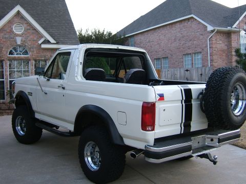 1991 Ford Bronco - This 1991 Ford Bronco features a classic white exterior with bold black racing stripes and a rear-mounted spare tire.