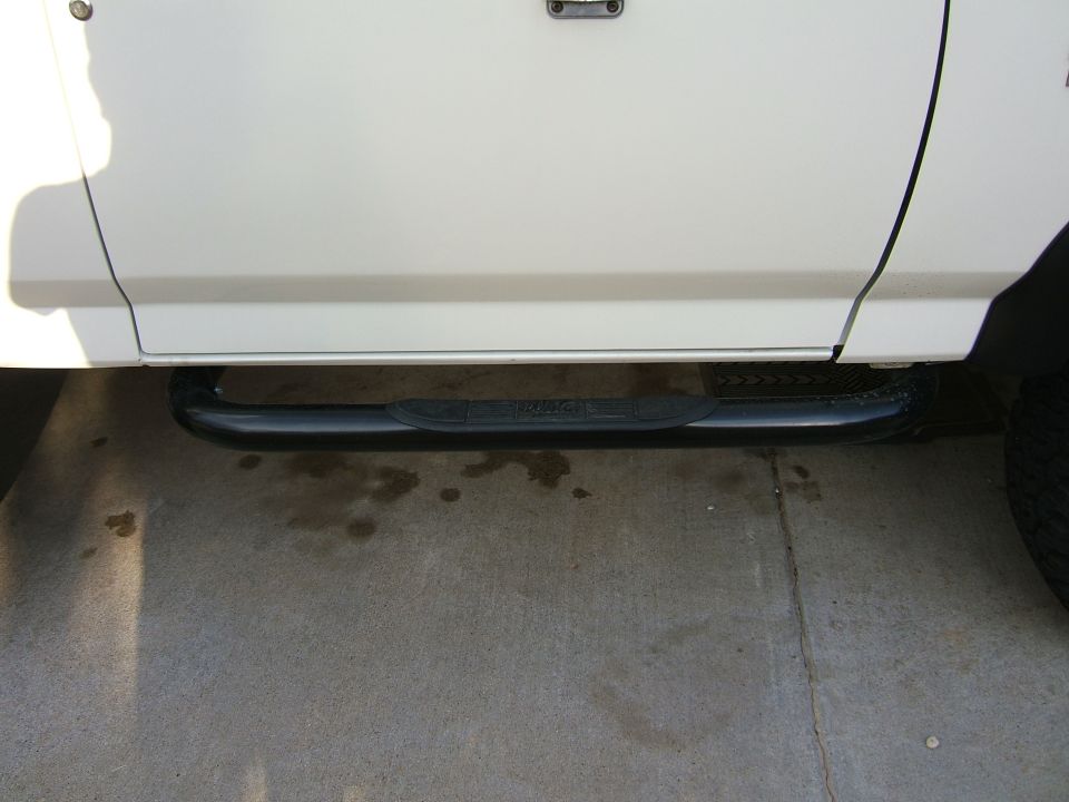 Black tubular side step bar with step pad mounted under the door of a white vehicle